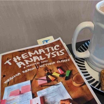 A photograph of the Braun and Clarke thematic analysis book next to a mug of tea and a piece of flapjack